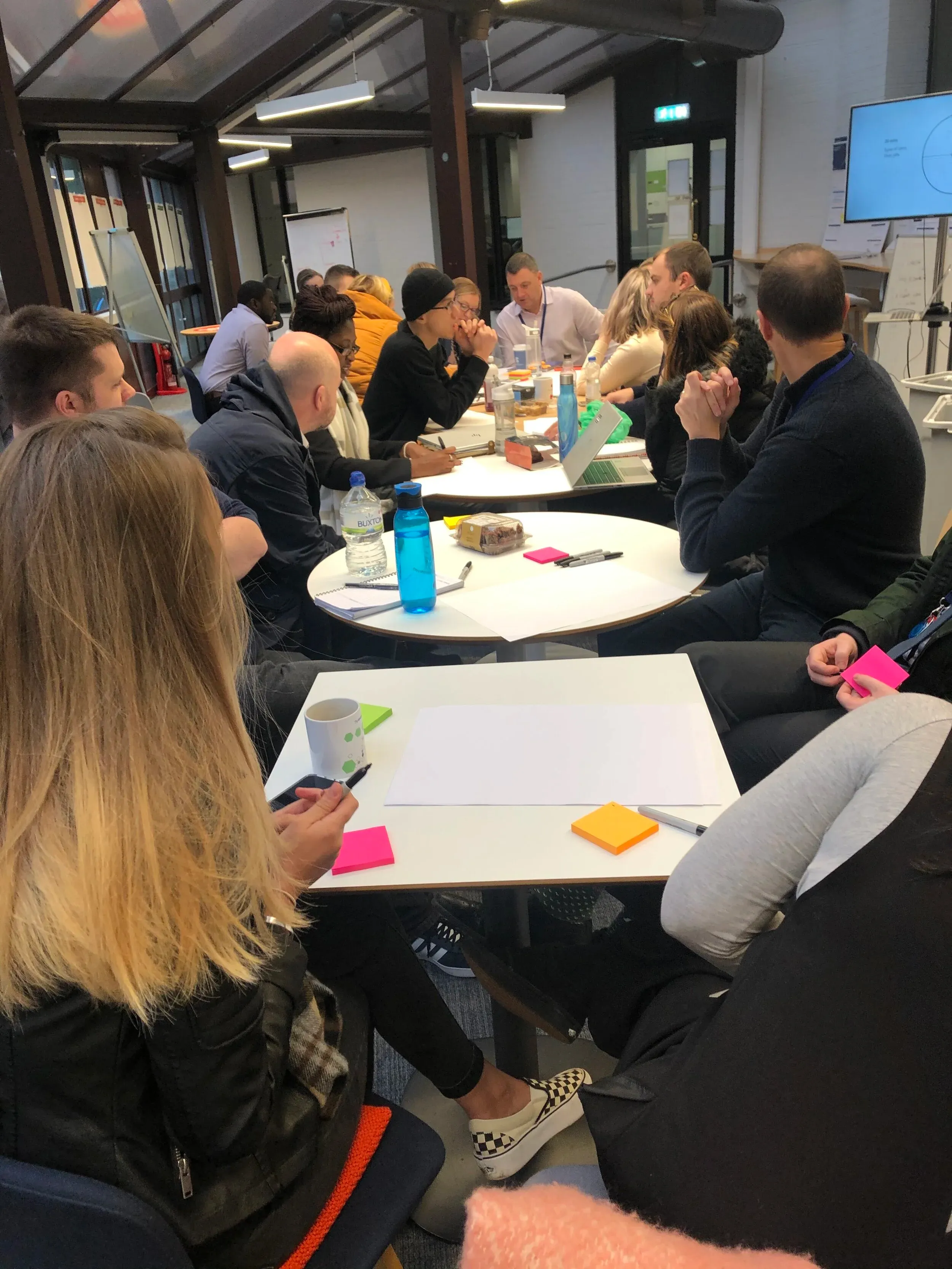 A briefing-day workshop: stakeholders from across the bank gathered around tables, sticky notes and a shared screen in play